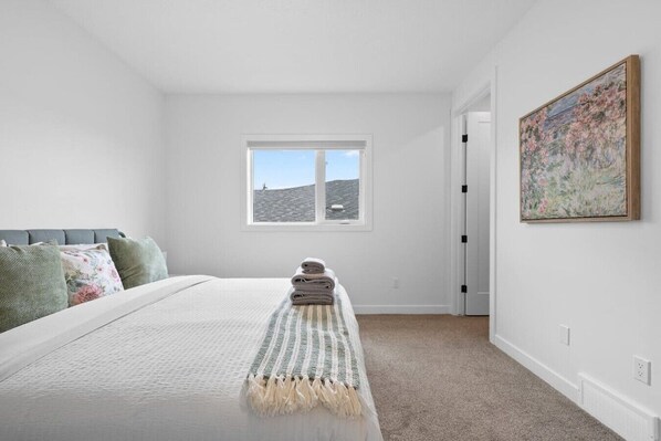 A bedroom with a bed, pillows, a window, a door, and a painting.