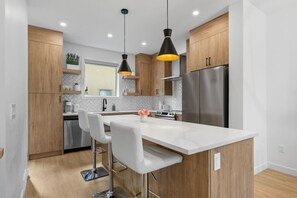Una cocina moderna con armarios de madera, un refrigerador de acero inoxidable, una isla de mármol blanco e iluminación colgante.