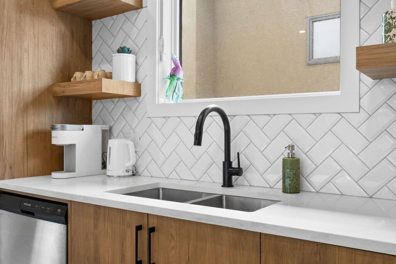Una cocina con diseño moderno, que incluye un lavamanos de acero inoxidable, una cafetera y un lavavajillas.