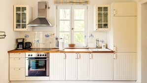 A kitchen with white cabinets, a stove, an oven, a window with curtains, and a tiled backsplash. - Charming semi-detached house in Trent on Rügen - Landhaus Trent Haushälfte Breet (Trent)
