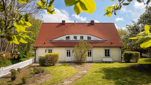 A two-story house with a red-tiled roof, a white fence, and a well-maintained lawn. - Charming semi-detached house in Trent on Rügen - Landhaus Trent Haushälfte Breet (Trent)