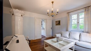 A living room with a white sofa, a glass coffee table, a white table, and a chandelier. - Charming semi-detached house in Trent on Rügen - Landhaus Trent Haushälfte Breet (Trent)