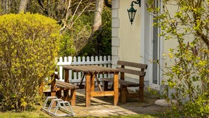 A wooden bench and table set against a white picket fence, with a building and trees in the background. - Charming semi-detached house in Trent on Rügen - Landhaus Trent Haushälfte Breet (Trent)