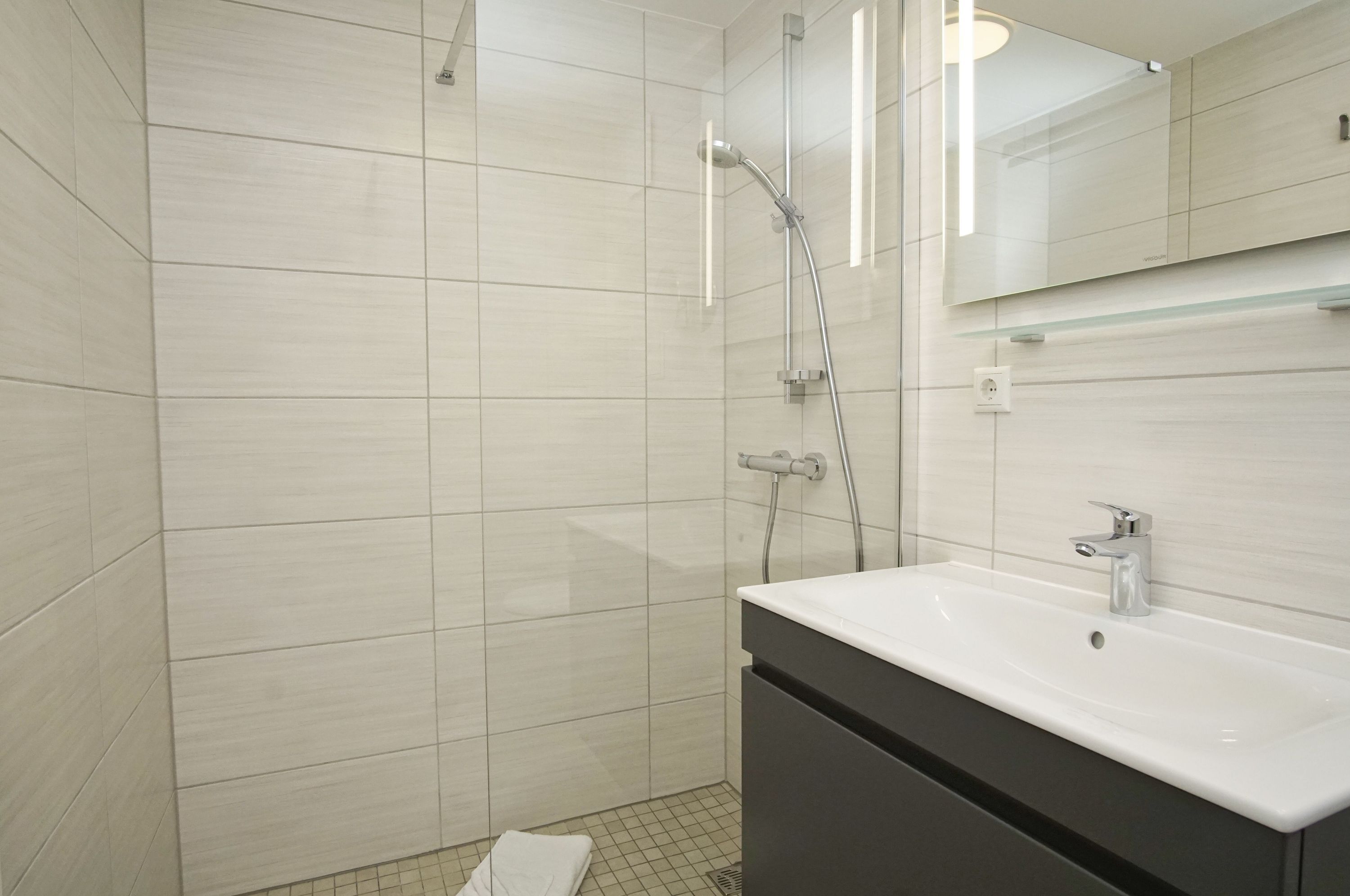 Une salle de bain moderne avec un lavabo blanc, un miroir et une douche.