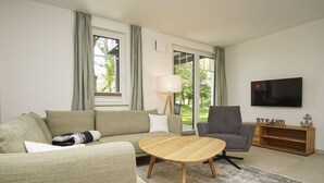 Un salon moderne comprenant un canapé, un fauteuil et une table basse, ainsi qu’un téléviseur et un buffet en bois.