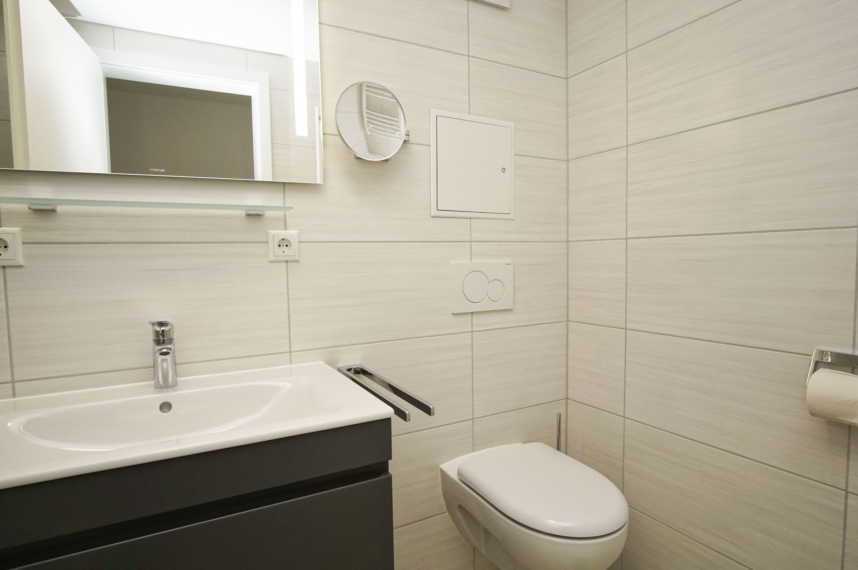 Un bagno moderno con lavandino, WC e specchio bianchi.