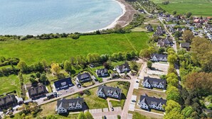 Vue aérienne d’une zone résidentielle côtière, avec des maisons, des champs verdoyants et une plage.