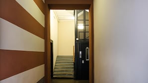 Kapea käytävä, jossa on portaikko, joka johtaa oveen, jossa on metallinen turvaverkko.