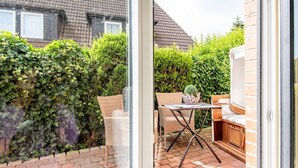 Eine Terrasse mit Tisch, Stühlen, einem Grill und einer Hecke.