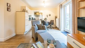 Ein kompakter Wohnbereich mit Sofa, Couchtisch, Fernseher, Küchenzeile und Esstisch.