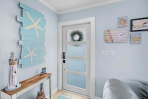 Une pièce avec une porte blanche, une décoration en forme d’étoile de mer, un petit phare et un tableau encadré accroché au mur.