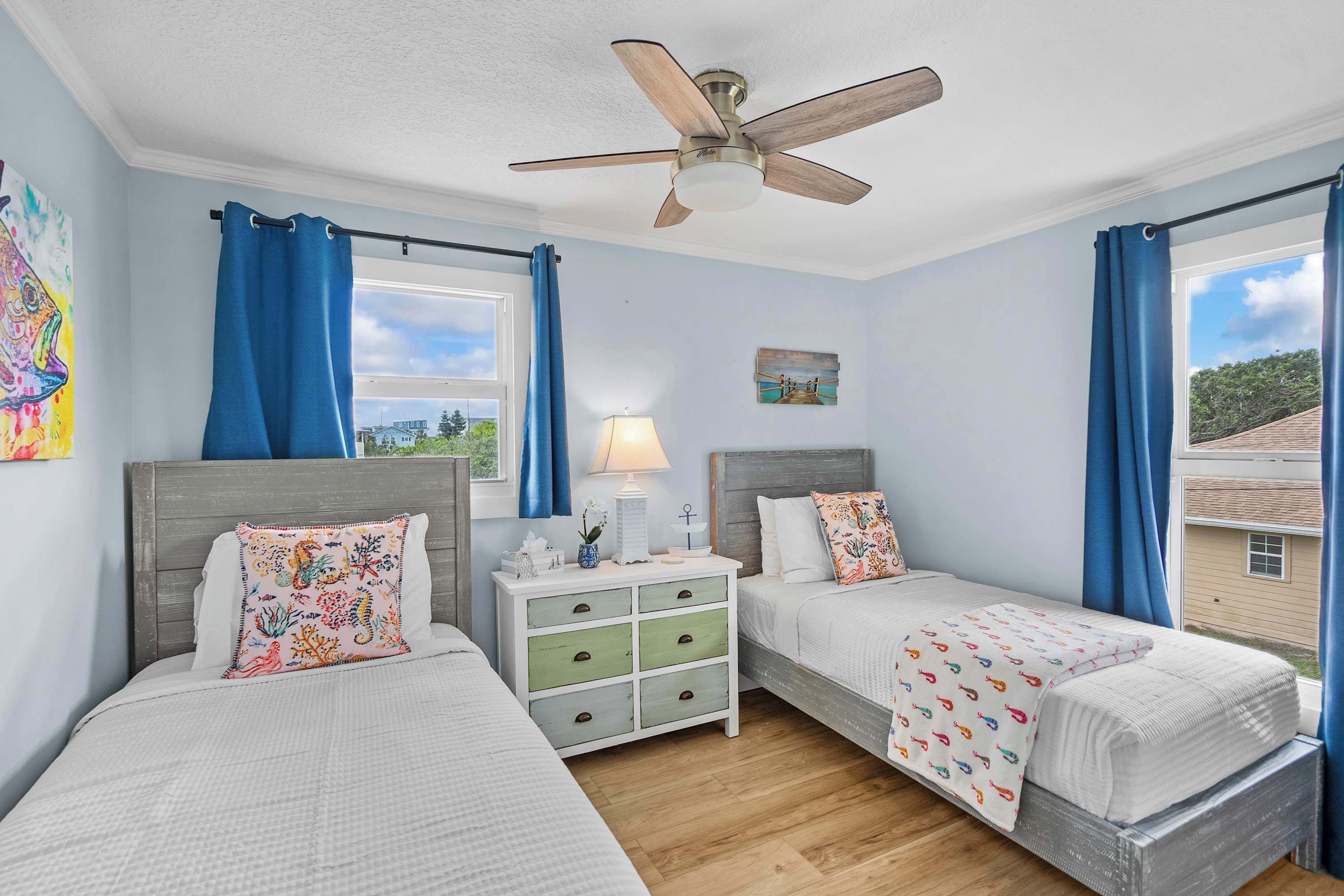 A bedroom with two beds, a ceiling fan, a nightstand, and a window with curtains.