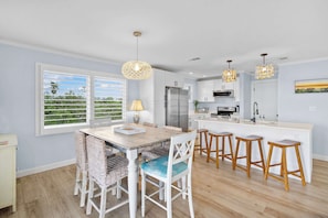 Une cuisine moderne avec des meubles blancs, un réfrigérateur en acier inoxydable et un coin repas comprenant des chaises en osier et une table en bois.