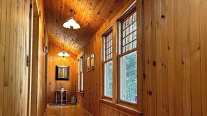 A wooden hallway with large windows, a framed picture on the wall, and a small table with a vase. - Forest Lodge Serenity on Long Lake - Dogs Welcome! (Traverse City)