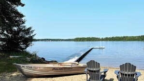 A boat named MC 0748 on a sandy shore with two Adirondack chairs facing the water. - Forest Lodge Serenity on Long Lake - Dogs Welcome! (Traverse City)