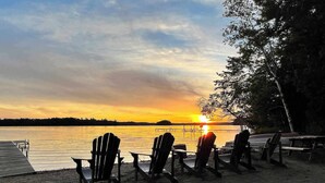 A sunset view with chairs and tables on a sandy shore. - Forest Lodge Serenity on Long Lake - Dogs Welcome! (Traverse City)