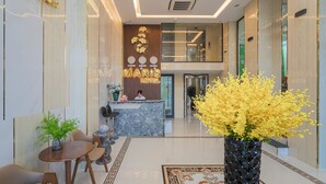 Eine Hotellobby mit einer Rezeption, einer Sitzecke und einer großen Vase mit gelben Blumen.