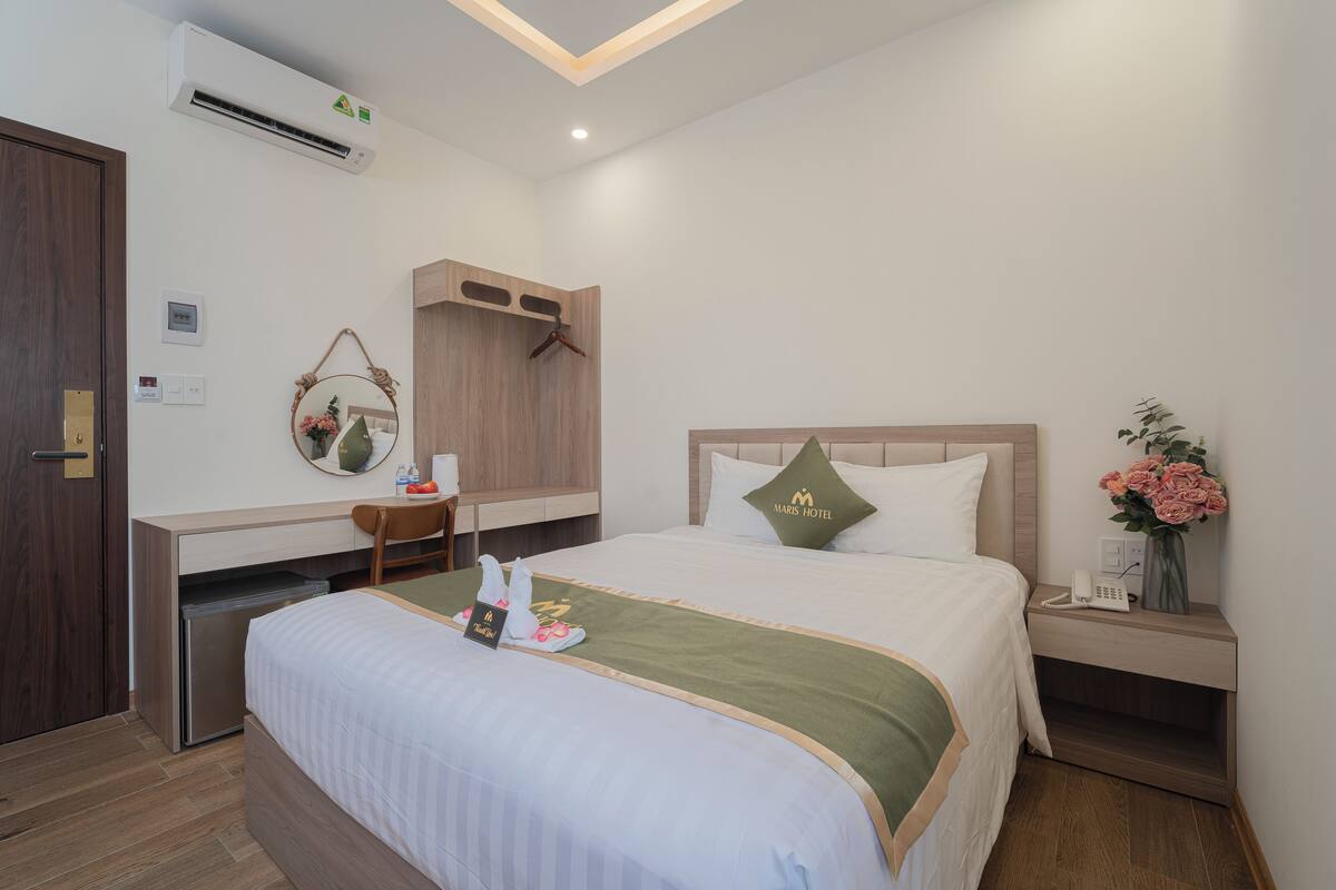 Ein Hotelzimmer mit Bett, Schreibtisch, Stuhl, Spiegel, Nachttisch und einer Wand-Klimaanlage.
