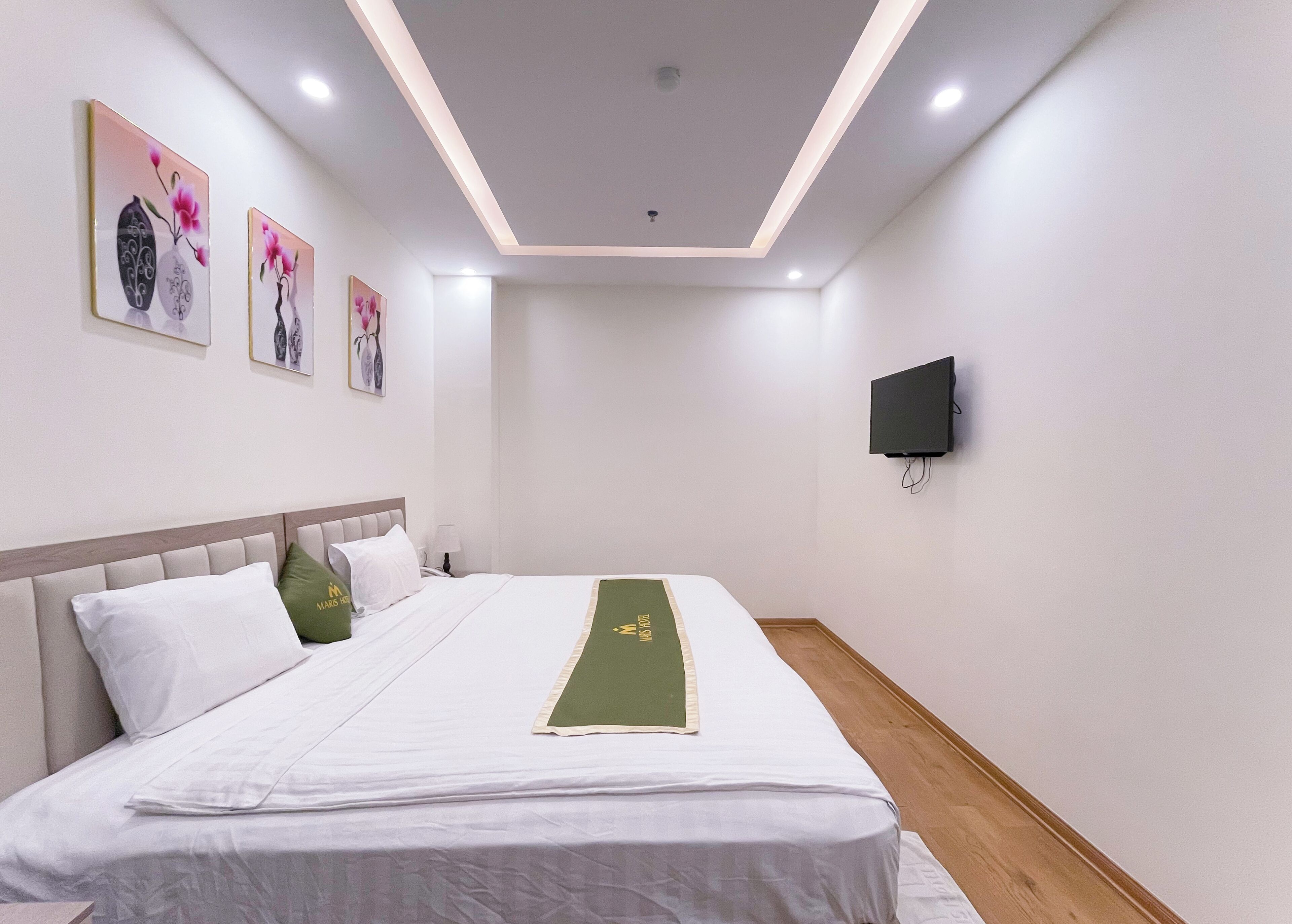 A hotel room with a bed, a flat-screen TV mounted on the wall, and artwork on the wall.