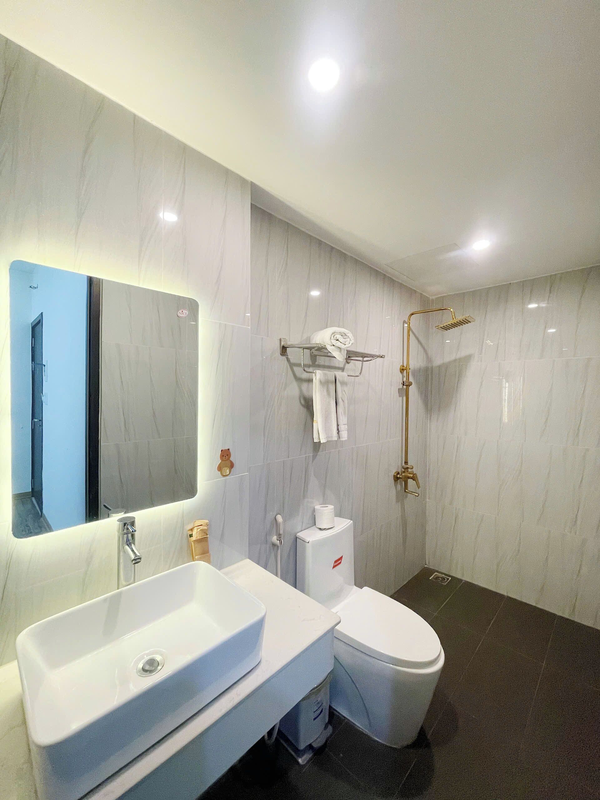 A modern bathroom with a large mirror, white sink, toilet, and a shower area.