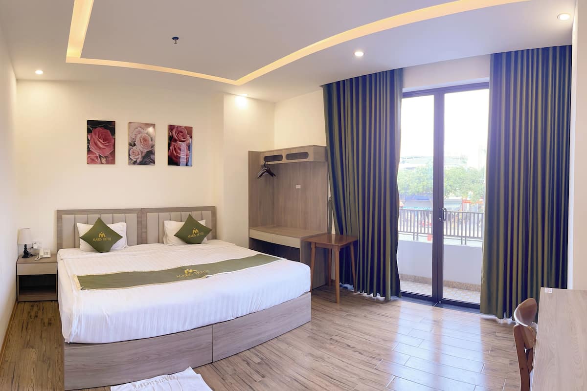 Ein Hotelzimmer mit einem großen Bett, einem Schreibtisch, einem Kleiderschrank und einem Balkon mit Vorhängen.