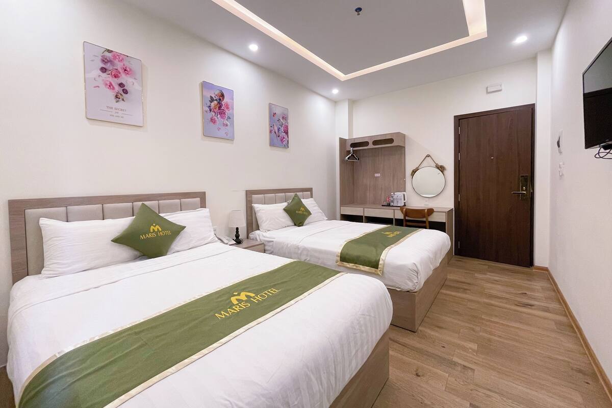 Ein Hotelzimmer mit zwei Betten, einem Schreibtisch, einem Spiegel und Bildern an den Wänden.