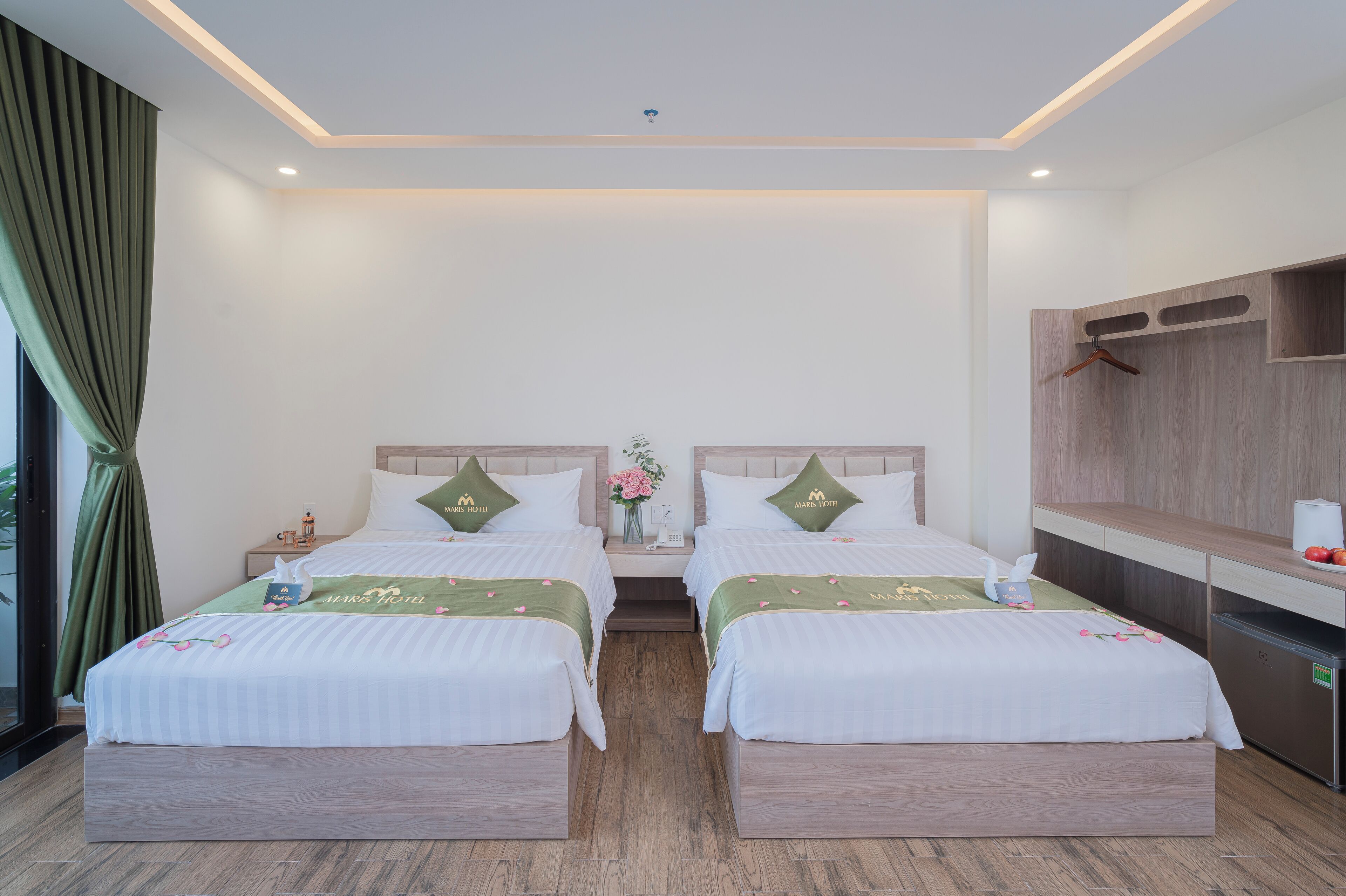 Habitación de hotel con dos camas, una mesita con un florero y un minibar.