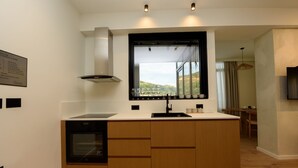 A modern kitchen with a built-in oven, a window with a view, and a dining area in the background. - E&K 01-02 Apartment (Vlorë)
