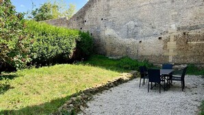 Un mur de pierres bordé d’un chemin de gravier menant à une table et des chaises disposées pour les repas en plein air.