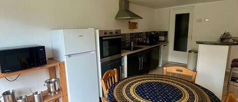A compact kitchen with a dining area, including a microwave, refrigerator, stove, and a round table with chairs.