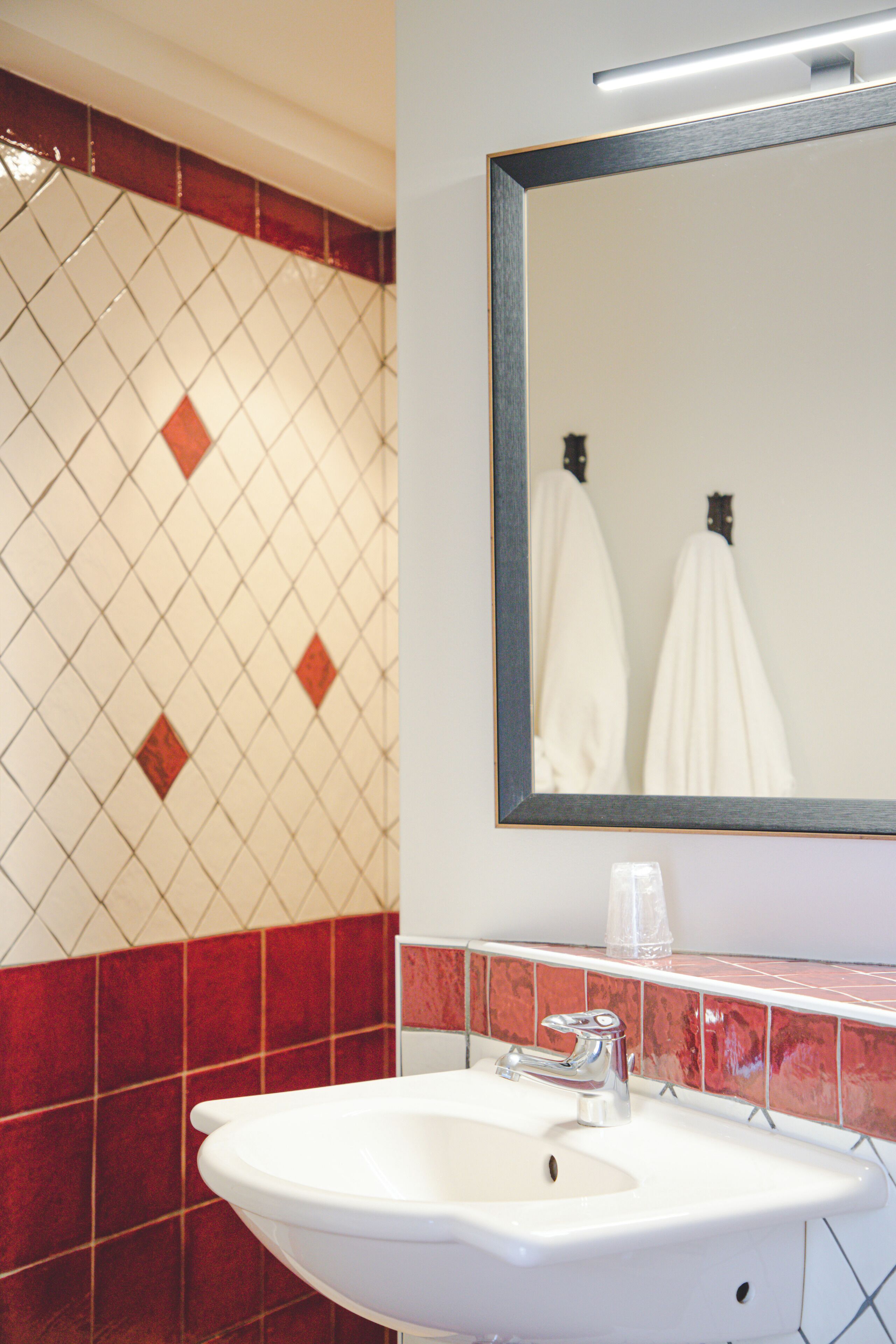 A bathroom with a white sink, red and white tiled walls, and a mirror above the sink.