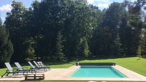 Une piscine rectangulaire dotée d’une terrasse dallée, entourée d’une pelouse bien entretenue et d’arbres.