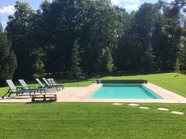 Une piscine rectangulaire dotée d’une terrasse dallée, entourée d’une pelouse bien entretenue et d’arbres.