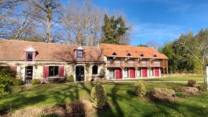 Un bâtiment traditionnel en pierre, avec un toit recouvert de tuiles rouges, plusieurs portes rouges et un balcon doté de balustrades en bois.