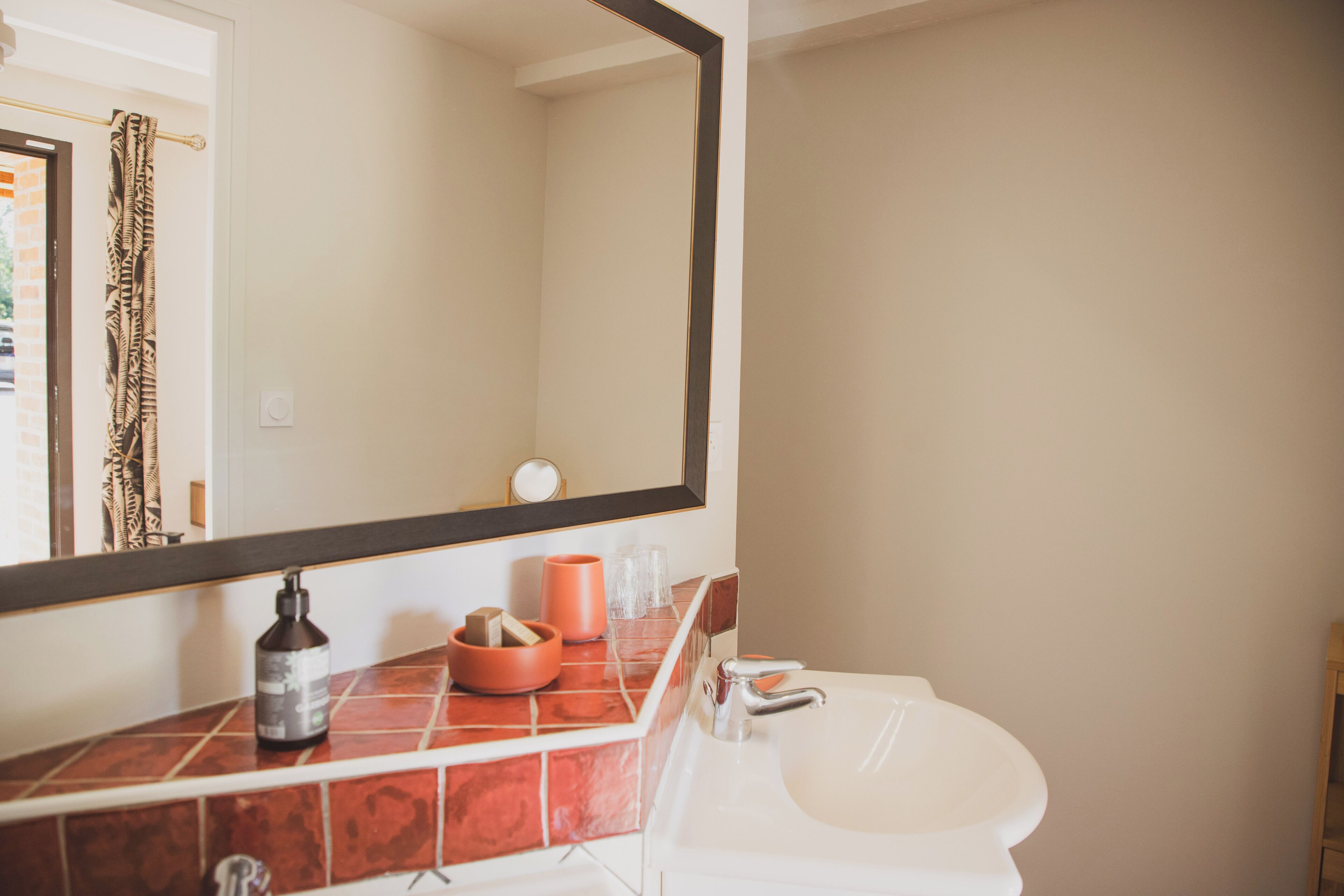 Un baño con lavamanos blanco, espejo y encimera azulejada.