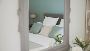 Un lit avec une literie blanche et verte, une lampe et un vase rempli de fleurs.