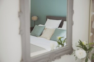 Un lit avec une literie blanche et verte, une lampe et un vase rempli de fleurs.