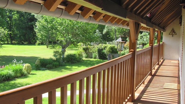 Un balcon en bois offrant une vue sur un jardin bien entretenu et des arbres.