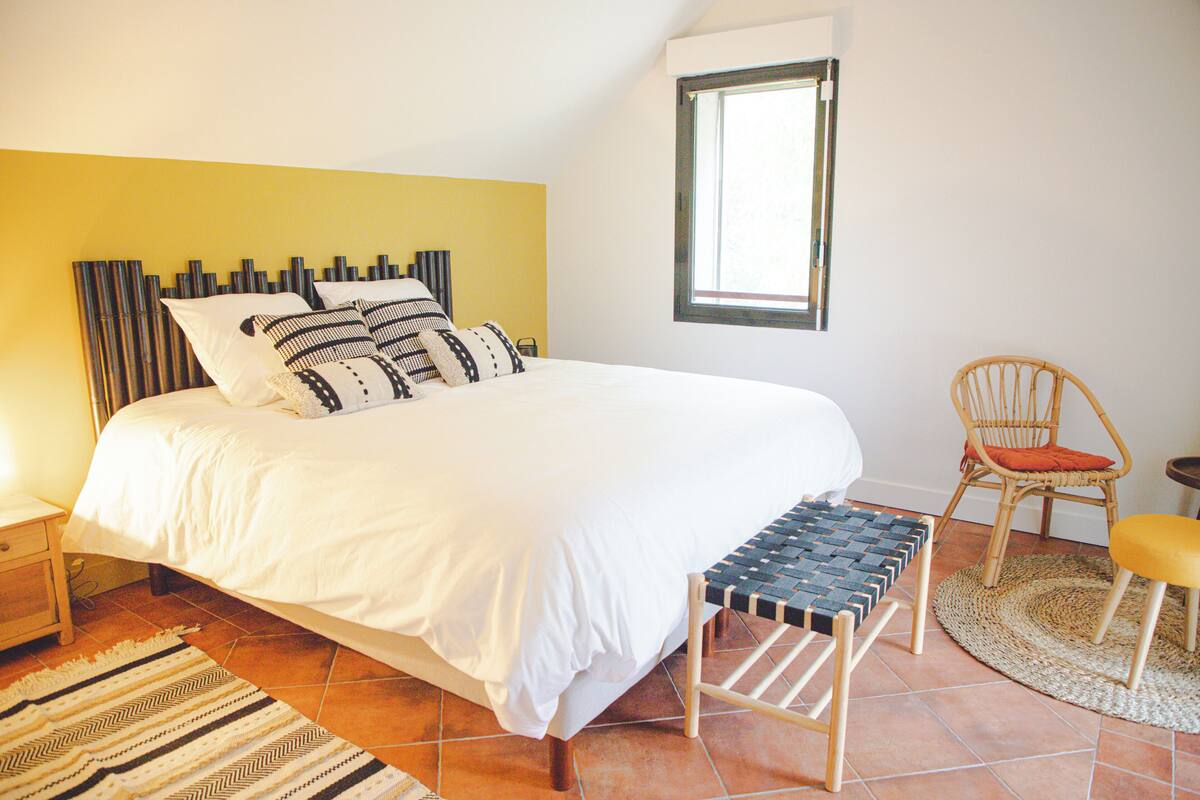 Een slaapkamer met een bed, een stoel, een bankje, een raam en een wand met een uniek ontwerp.