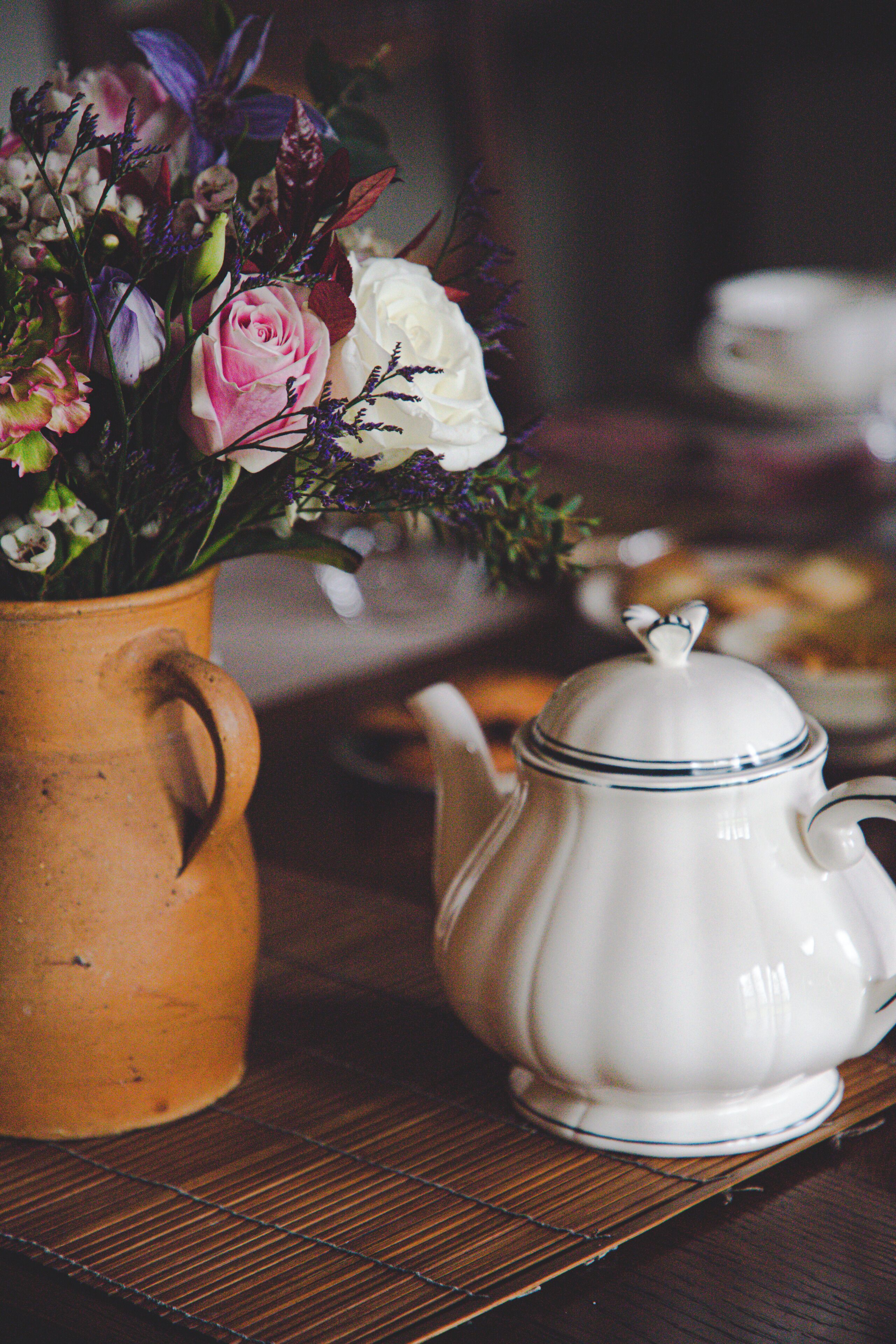 A ceramic teapot and a vase with flowers on a wooden surface.