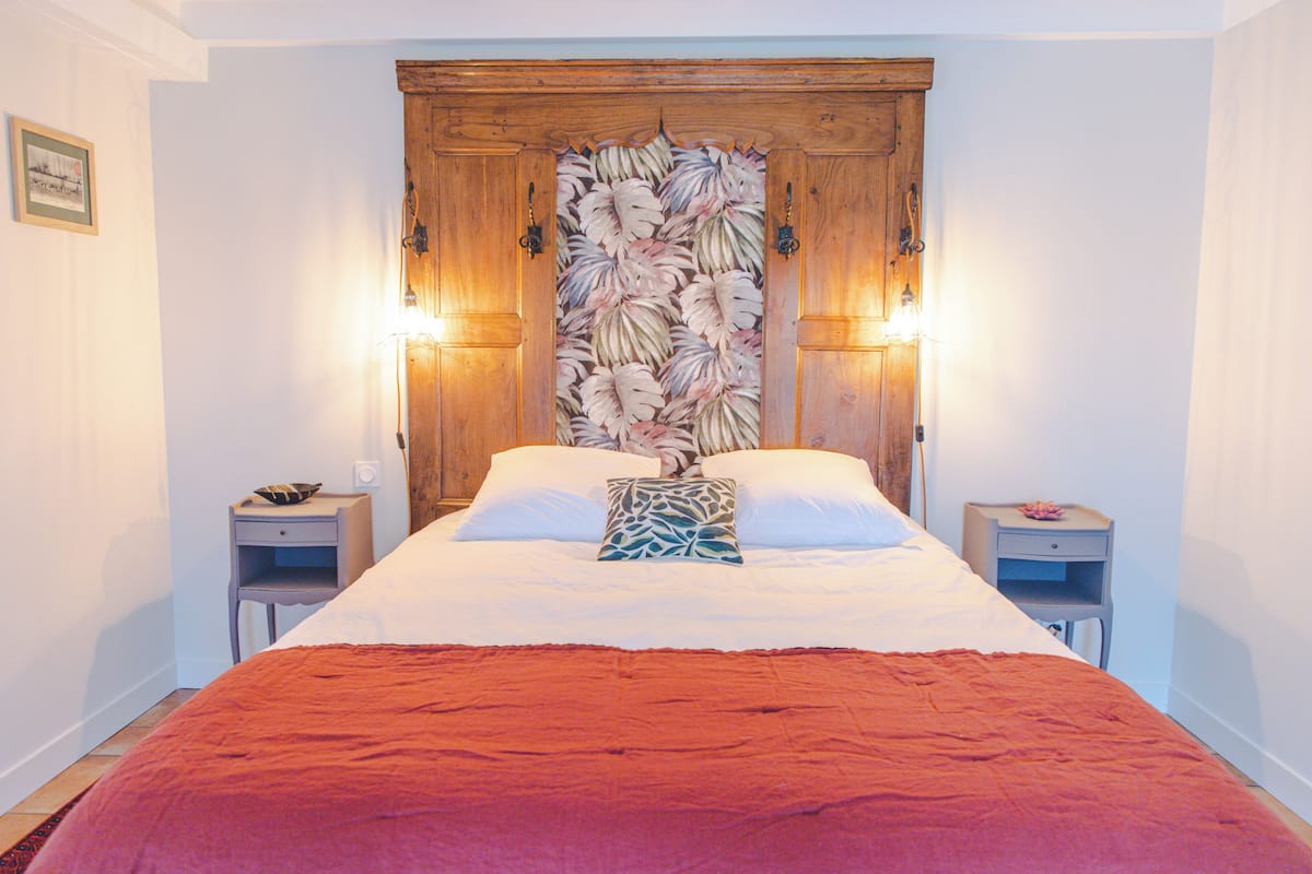 Een slaapkamer met een groot bed, twee nachtkastjes, een houten hoofdbord met een bladmotief en wandlampen.