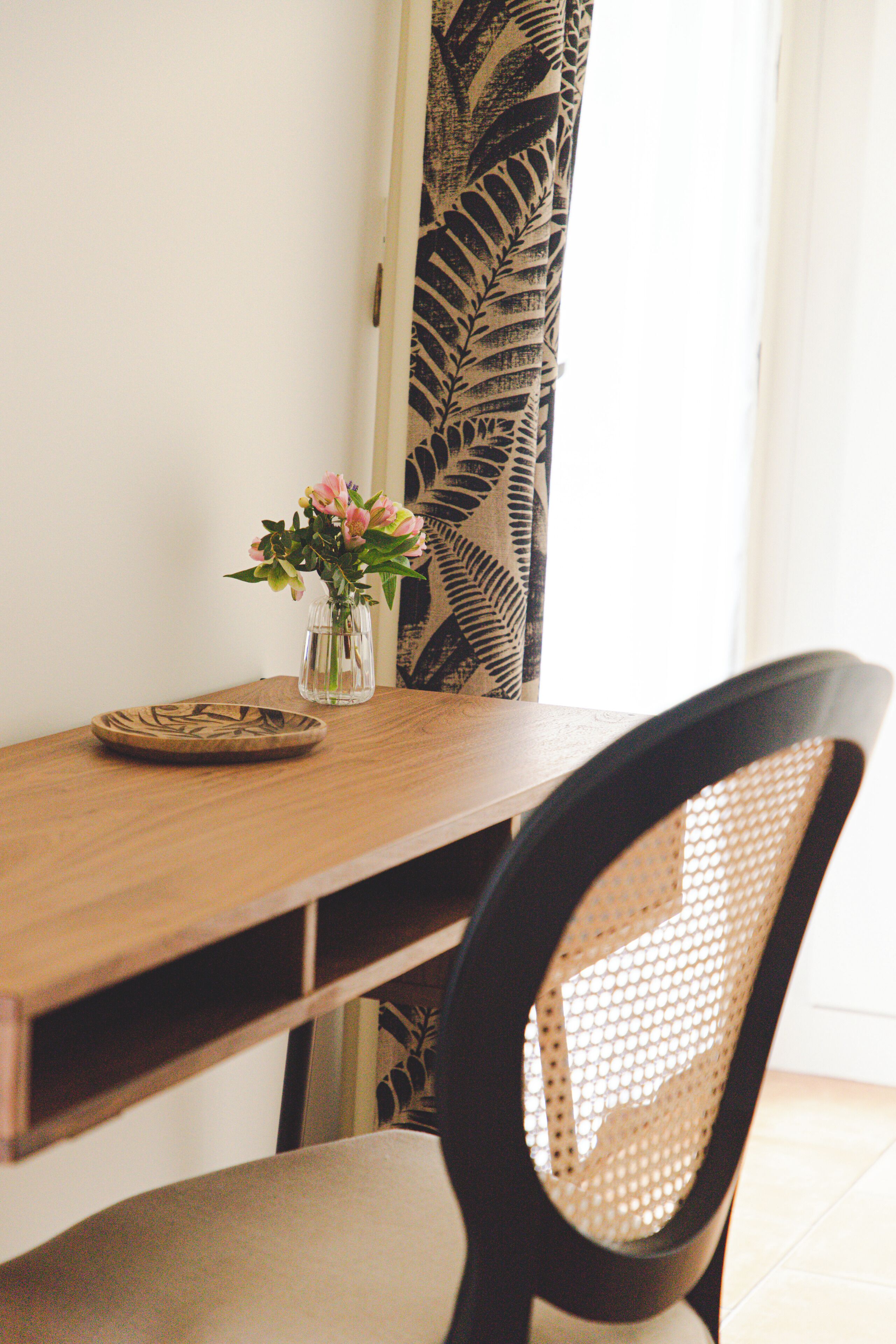A wooden table with a vase of flowers and a woven placemat.