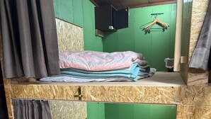 A bunk bed room with green walls, a wooden floor, and a small shelf with folded clothes.