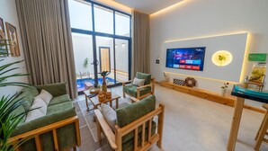 Una sala de estar moderna con un televisor grande, muebles verdes y vistas a una piscina.