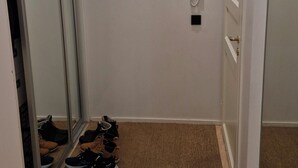 Een gang met een houten vloer, een vloermat met tapijt, een telefoon en een deur.