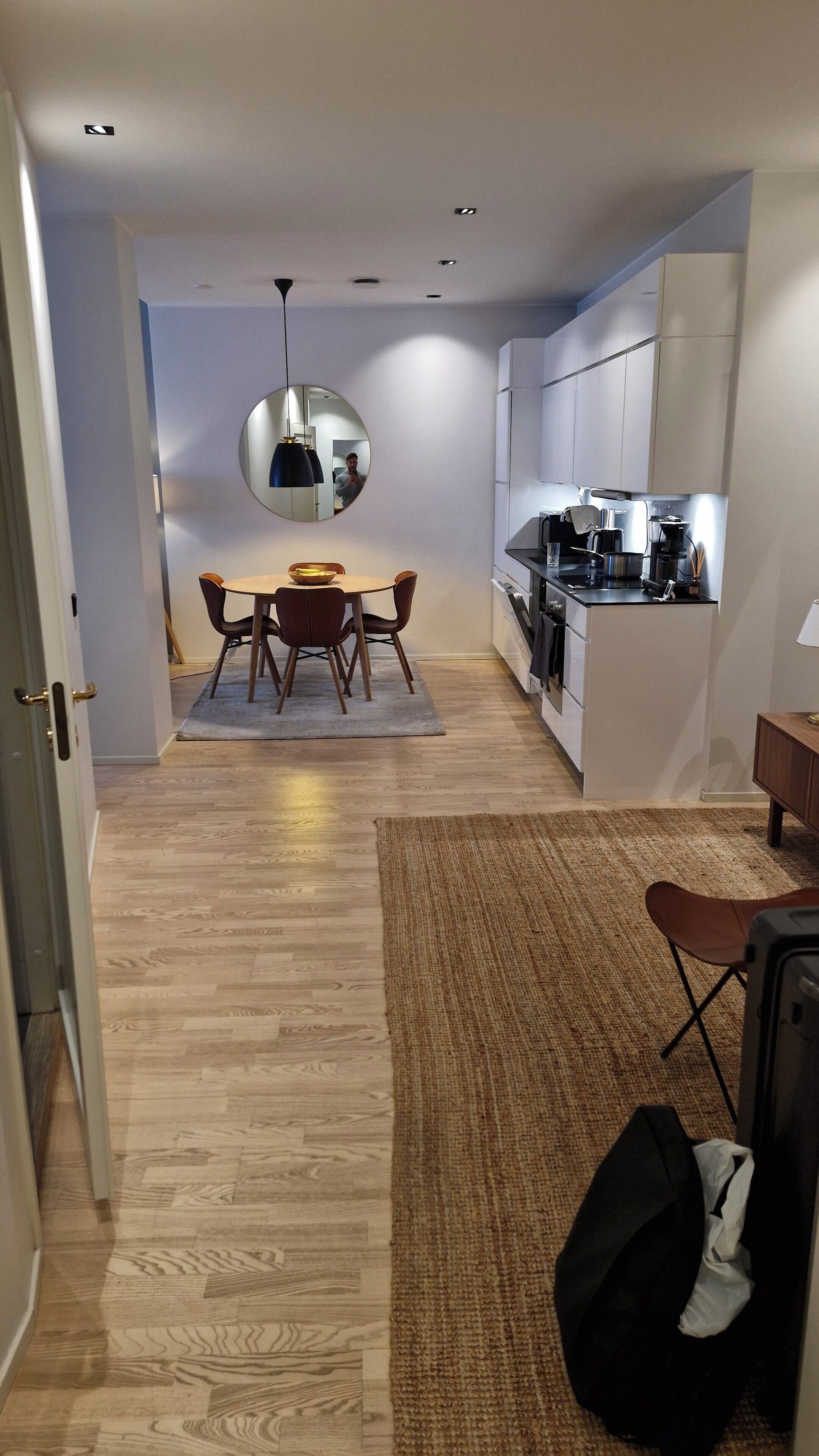 Een moderne keuken met witte kasten, een eethoek met een ronde tafel en stoelen, en een hal met houten vloeren.