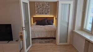 Een slaapkamer met een bed, een televisie en een raam met zonwering.