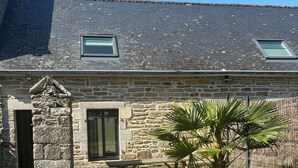 A stone building with a sloped roof, a stone chimney, and a wooden bench in the yard. - Typical Breton house "Ty Breizh" Beg Meil Fouesnant plage des oiseaux (Fouesnant)