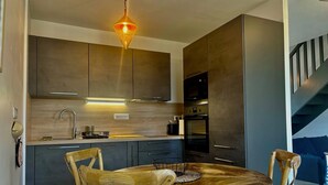 A modern kitchen with dark cabinets, a wooden dining table, and a hanging light fixture. - Typical Breton house "Ty Breizh" Beg Meil Fouesnant plage des oiseaux (Fouesnant)