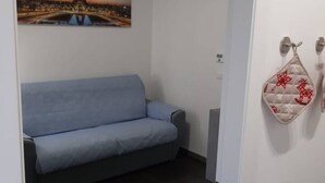 Huoneessa on sininen sohva, seinään kiinnitetty patteri ja koriste-esine, jossa on punaisia kuvioita.